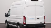 Rear view of a white Ford Transit cargo van shown from the back-left, with double rear doors and black bumper indoors.