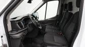 Interior of a white van showing driver and two front passenger seats, steering wheel, and dashboard with cup holder far left.