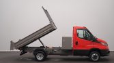 Red dump truck with cargo bed raised for unloading, hydraulic system visible beneath bed similarity to tilt-bed trucks