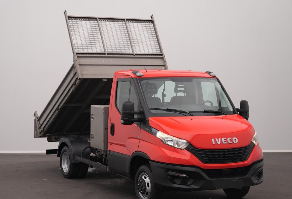 Red Iveco dump truck with its bed raised for dumping against a plain gray background.