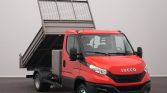 Red Iveco dump truck with its bed raised for dumping against a plain gray background.