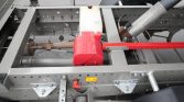 Close-up of a gray metal chassis with a red plastic reservoir, hydraulic hoses, and a large cylindrical actuator on the right.