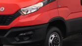 Red van front-left view showing headlight, grille, and wheel; cargo van design with black bumper and side panel details
