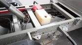 View of a trailer chassis showing a plastic coolant reservoir, red toolbox, hydraulic hoses, and metal frame with hitch assembly.
