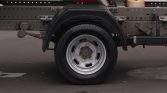 Close-up of a truck trailer wheel: silver rim, black tire, and gray fender with the undercarriage and frame.