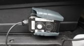 Trailer brake controller mounted under a vehicle dashboard with two round buttons and a gray protective cover, wired to the car's electrical system.
