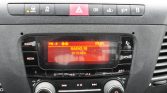 Orange backlit car radio display showing RADIO 10, 97.70 MHz, time 03:01, with surrounding control buttons and knobs.