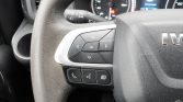 Steering wheel left-side control pad with directional arrows and OK button, plus phone and menu buttons; dashboard gauges in the background.