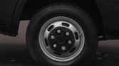 Close-up of a car wheel: silver steel rim with six lug nuts on a dark vehicle, tire mounted, photographed on a paved surface.