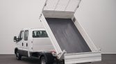 White dump truck with raised tipping bed in a studio setting, showing the load bed angled upward for dumping