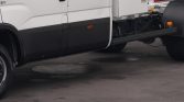 Side view of a white cargo truck showing the black lower body panel, wheel, and exposed rear chassis on a paved surface.