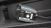 Portable car jump starter/booster pack clipped to a vehicle battery area with gray protective clamps open