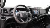 Dashboard interior of a left-hand-drive vehicle: steering wheel with control buttons, instrument cluster, center touchscreen, climate controls, and gear shifter visible on the console.