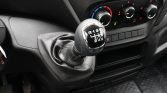 Manual gear shift lever in a car, wrapped in leather with a six-speed pattern and reverse gear visible atop the console surface in front of the driver seat.