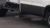 Side view of a white semi-truck showing lower door panel, orange marker light, and exposed undercarriage near the front wheel.