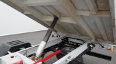 Hydraulic lift mechanism under a dump truck bed, showing a gas strut and metal chassis with a red fuel can in the foreground.