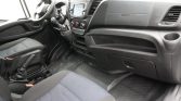 Front interior of a black van: driver seat, steering wheel, center console with touchscreen, gear shifter, and dashboard visible above a rubber floor mat