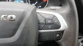 Close-up of the right side of a car steering wheel showing cruise control buttons (SET+, SET−, RES, CANCEL) with a silver trim; instrument gauges visible in the background.