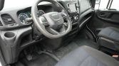 Driver's area of a vehicle showing steering wheel, instrument cluster, center touchscreen, manual gear shifter, and black fabric seats.