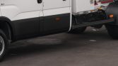 Side view of a white commercial truck with black lower body panels and exposed chassis near the cab's door
