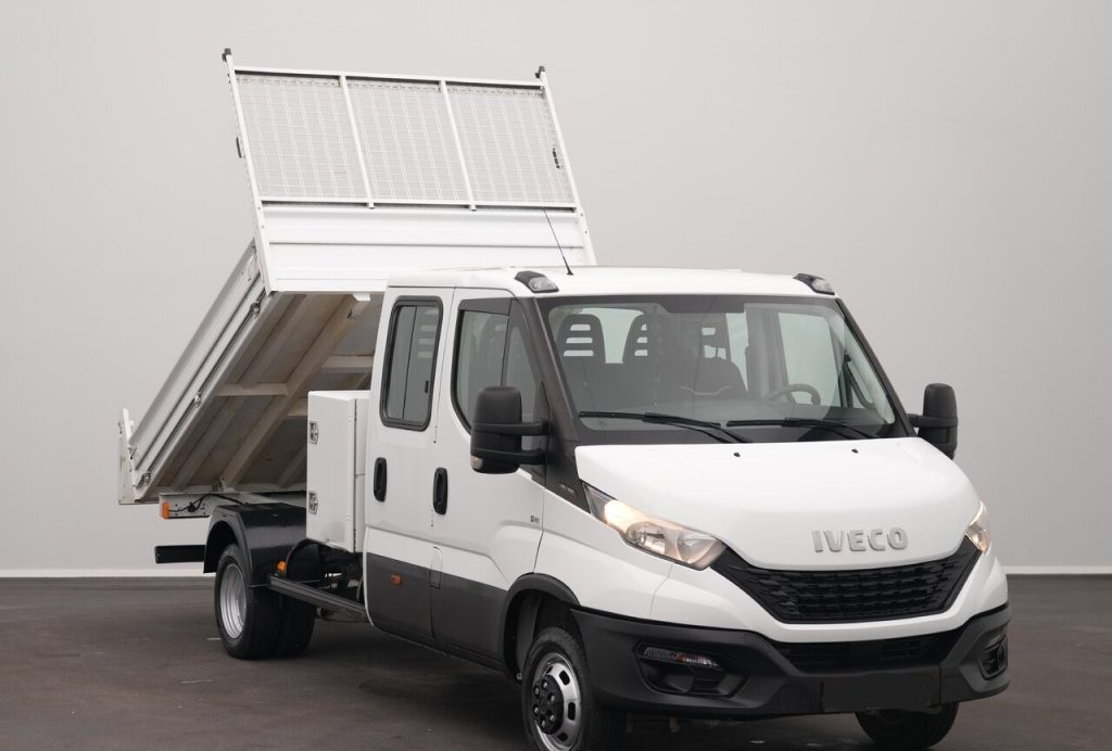White Iveco utility truck with a raised dump bed behind the cab, parked indoors.
