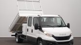White Iveco utility truck with a raised dump bed behind the cab, parked indoors.