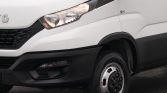 Close-up of a white van front showing the headlight, grille, and front-right wheel.