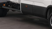 Side view of a white commercial truck with a black lower panel; a deployed run-off-style step extends from the cab area toward the ground.