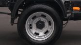 Close-up of a truck wheel with silver steel rim and black tire under a fender, showing lug nuts and an orange side marker light