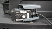 Portable car jump starter attached to a vehicle battery, with two round buttons and a cord plugged in.