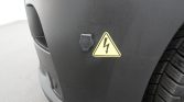 Vehicle bumper with a yellow high-voltage warning triangle sticker (lightning bolt) near the wheel area.