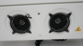 Two black circular cooling fans with protective grills mounted side by side on a white surface, likely outdoor HVAC equipment.