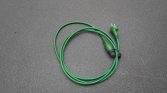 Green electrical extension cord coiled on a dark asphalt surface, with plug end visible on the right side of the image.