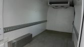 Empty white cargo trailer interior with metal anchor rails along both walls and a ceiling-mounted air conditioner; two metal blocks on the floor.
