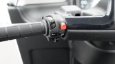 Scooter left handlebar controls with textured grip, red engine-stop button, horn, and turn-signal switch.