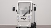 Front view of a small white delivery vehicle with round headlights and a logo that reads 'garry' on the hood. Two side mirrors extend from the cabin.