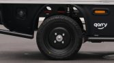 Close-up of a black truck wheel on a small delivery vehicle, showing the tire, hub, and surrounding chassis with a 'qarry' branding panel nearby.