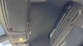 Interior of a van cabin ceiling with overhead light switch on and folded sun visors visible to the left and right of the roof panel