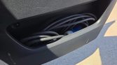 Open car door storage pocket containing coiled black cables, with a blue connector visible.