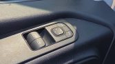 Close-up of a car's driver-side door controls: two window switches and a round mirror-adjustment joystick with lock button nearby on a black textured panel