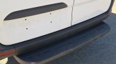 White van rear showing a black plastic step bumper with an empty license plate area and several mounting holes, plus dirt marks on the tailgate.