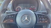 Mercedes-Benz steering wheel with built-in audio and control buttons, logo centered, dashboard visible in background.