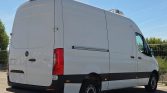 White high-roof cargo van with a rooftop refrigeration unit, viewed from the rear-right, parked on a lot.
