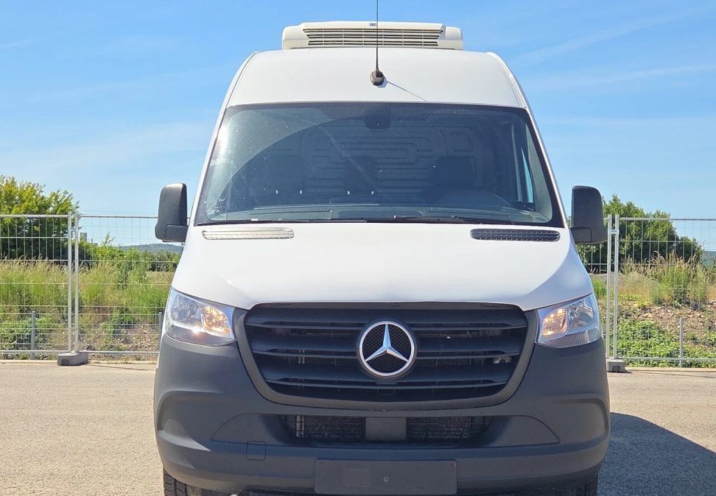 Front view of a white Mercedes-Benz cargo van with a black grille and roof air conditioner, parked outdoors on a sunny day.