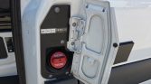 Open fuel cap door on a white truck, red diesel filler cap labeled DIESEL visible in a black panel area.