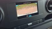 Rearview camera display showing parking area with red guiding lines and a fence in the background.