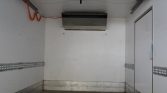 Empty white cargo trailer interior with metal side rails, a doorway on the right, and an overhead cooling unit; orange cord along the left wall.