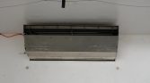 Ceiling-mounted HVAC indoor unit with its front panel removed, exposing coils and internal components by a white wall.
