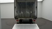 Rear view of a delivery truck with its cargo area open, a metal loading ramp extended to the ground, and red tail lights visible on both sides.