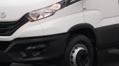 Close-up of the front section of a white panel van, showing the headlight, black bumper/grille, and the front wheel.